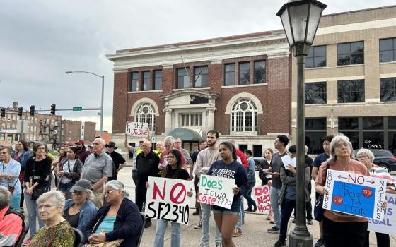 People holding signs demonstrate in square, with brick buildings in background. 