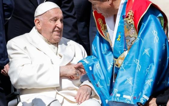 Pope Francis, from wheelchair, shakes hands with audience wearing vibrant, traditional garb.