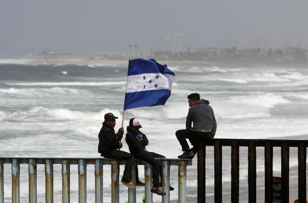 People hold a Honduran flag while sitting on the border fence between Mexico and the United States in Tijuana, Mexico, April 29. The Trump administration is ending temporary protected status for more than 50,000 Hondurans. (CNS/Reuters/Jorge Duenes)