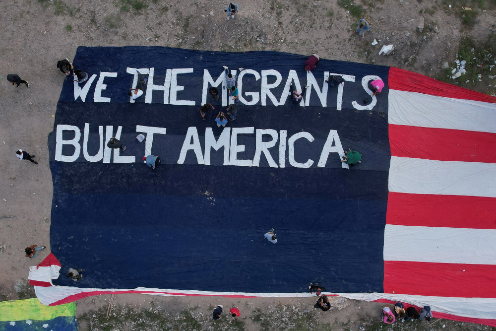 A banner of a US flag that says "We the migrants built America"