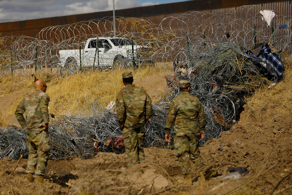 Members of the Texas National Guard stand near a razor wire fence used to prevent migrants from crossing into the United States, along the Rio Bravo, at the U.S.-Mexico border, as seen from Ciudad Juárez, Mexico, Jan. 22. (OSV News/Reuters/Jose Luis Gonzalez)