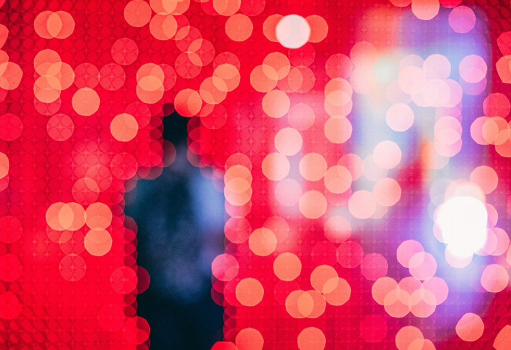 An abstract photo illustration shows out of focus red lights creating an outline of a person. (Unsplash/Guillaume Bourdages)