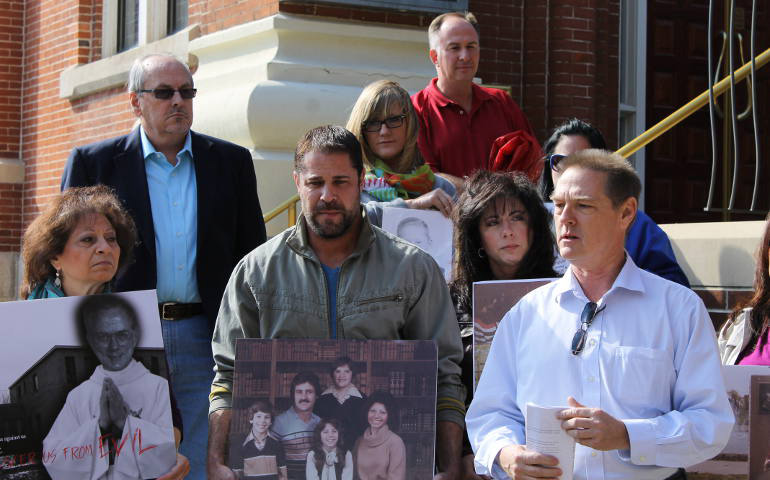 Jon David Couzens, center, holds a family photo from his childhood during a press conference Friday outside the Cathedral of the Immaculate Conception in Kansas City, Mo. (NCR photo/Brian Roewe) 