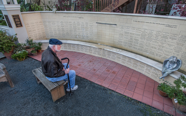 Pete Toms, coordinator of Most Holy Redeemer's AIDS support group, looks at the memorial wall in a garden behind the church. (Dennis Callahan)
