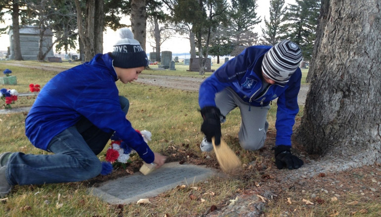 Ryan Fenley (left) and Trace Martin clean the headstone of a veteran's grave at Mount Calvary Cemetery in Lewistown, Montana. The pair are members of St. Leo Parish junior high youth group. (Photo courtesy of The Harvest)