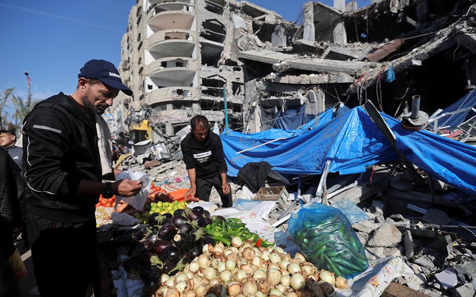 A Palestinian vendor prepares his products in an open-air market in the Nuseirat refugee camp in the central Gaza Strip Nov. 30 near the ruins of houses and buildings destroyed in Israeli airstrikes during the Hamas-Israel conflict, amid a temporary truce between Hamas and Israel. (OSV News/Reuters/Ibraheem Abu Mustafa)