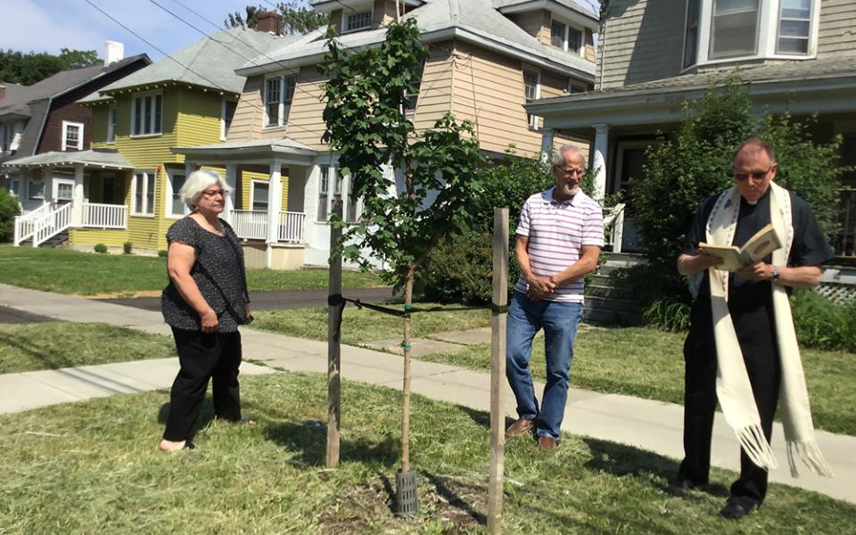 Fr. Frederick Daley, pastor of All Saints Church, blesses a tree planted by some of the members of the Caring For Our Common Home environmental task force in Syracuse, New York, in summer 2023. (Courtesy of Michael Songer)