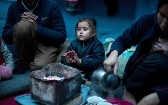 A girl is pictured in a file photo warming her hands over hot coal next to her parents inside their temporary shelter on the island of Lesbos, Greece. 