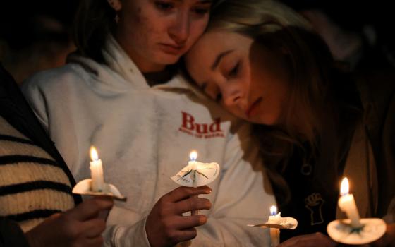 One person leans on another as they hold candles