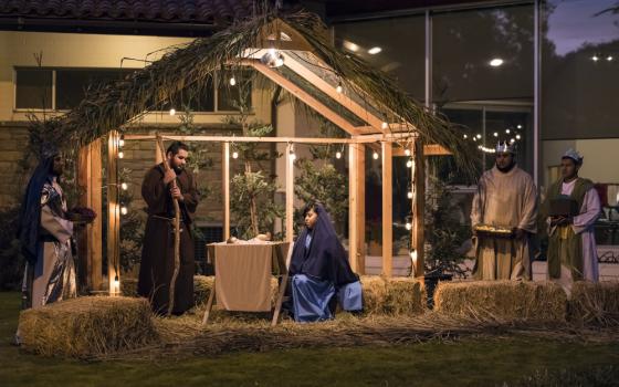 People sit in an outdoor nativity scene illuminated in the evening