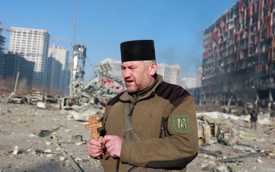 Mykola Medinsky, a Ukrainian Orthodox military chaplain, prays with a crucifix and prayer beads at the site of a Russian military strike on a shopping center in Kyiv March 21, 2022. (CNS photo/Serhii Nuzhnenko, Reuters)