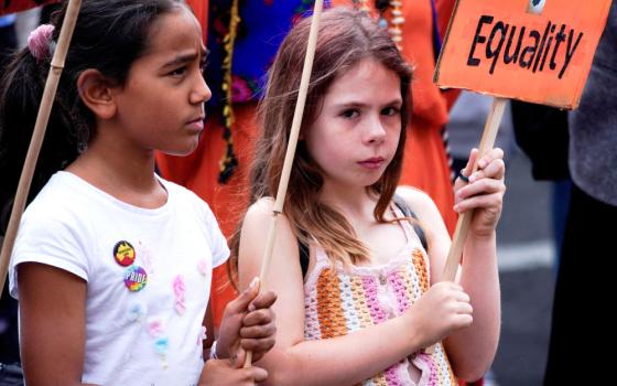 Two young girls stand side by side. One holds a sign that says "Equality."