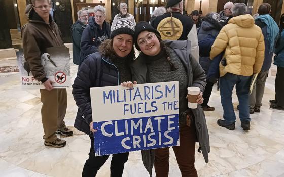 Chrissy Kirchhoefer, left, and Lindsey Myers, St. Louis-area Catholic Workers, hold a sign during a witness in the Wisconsin State Capitol in Madison on March 27. (NCR photo/Theodore Kayser)
