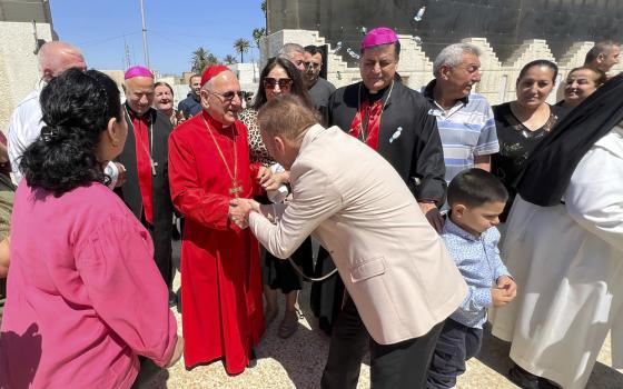 Cardinal, wearing red clerical garb, greets joyful crowd in street. 
