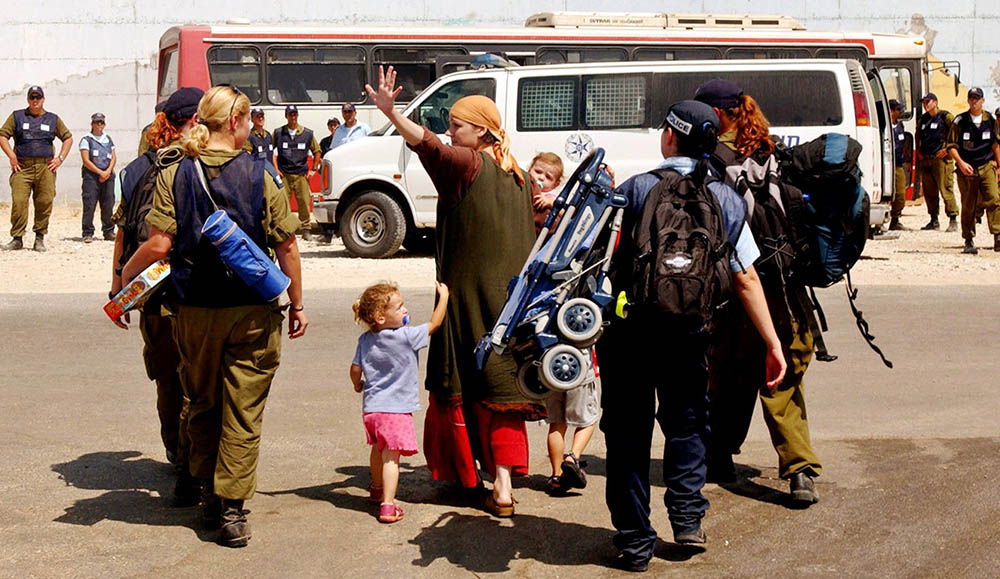 A Jewish settler waves as she and her family are escorted to a bus by Israeli soldiers and police officers during the forced evacuation of the Jewish settlement of Morag in the Gush Katif settlement bloc in the Gaza Strip Aug. 17, 2005. (CNS/Reuters)
