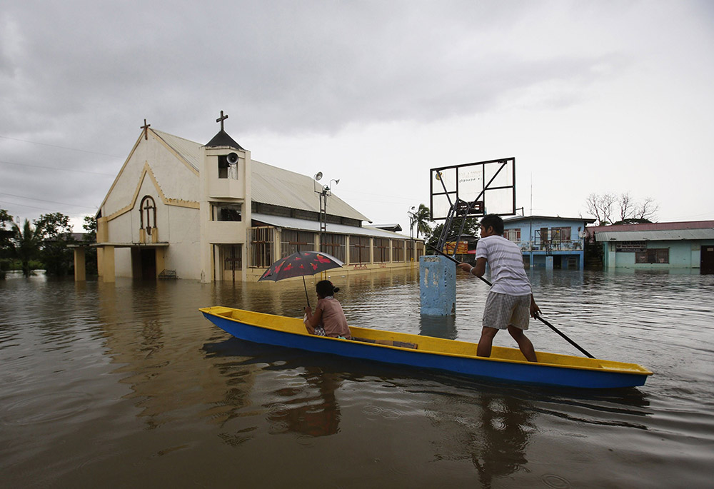 People make their way by boat past a church along a flooded road in Bulacan, Philippines, Aug. 21, 2013, following heavy monsoon rains. (CNS/Reuters/Erik de Castro)