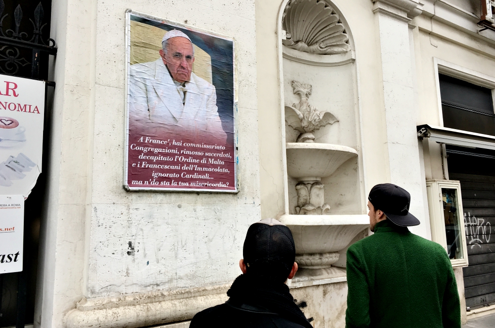 People look at a poster expressing criticism of Pope Francis in Rome Feb. 5, 2017. Numerous copies of the poster were placed in the center of Rome but were quickly covered or removed by city authorities. (CNS/Paul Haring) People look at a poster expressing criticism of Pope Francis in Rome Feb. 5, 2017. Numerous copies of the poster were placed in the center of Rome but were quickly covered or removed by city authorities. (CNS/Paul Haring)