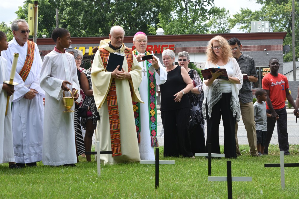 Fr. Victor Clore and members of Christ the King Parish in Detroit pause for a moment of silence July 22, 2017, in front of 44 crosses on the parish's front lawn, one for each of the lives lost in the city's violence of 1967. (CNS/The Michigan Catholic)