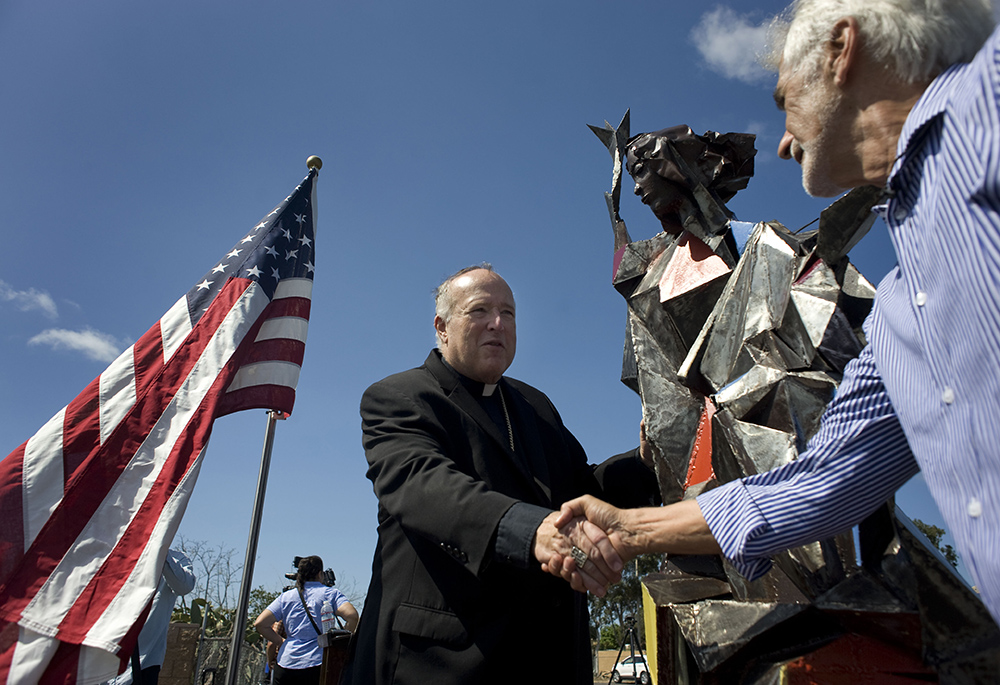San Diego Bishop Robert McElroy greets artist Jim Bliesner Oct. 5, 2018, next to a miniature replica of a statue Bliesner is creating in honor of immigrants and refugees during a ceremony in San Diego. (CNS/David Maung)