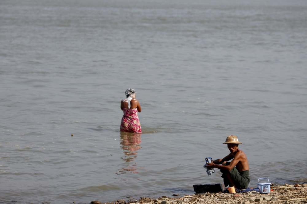 A man washes clothes and a woman washes her hair along the bank of the Irrawaddy River in Sagaing, Myanmar in 2012. (CNS/Reuters/Soe Zeya Tun)