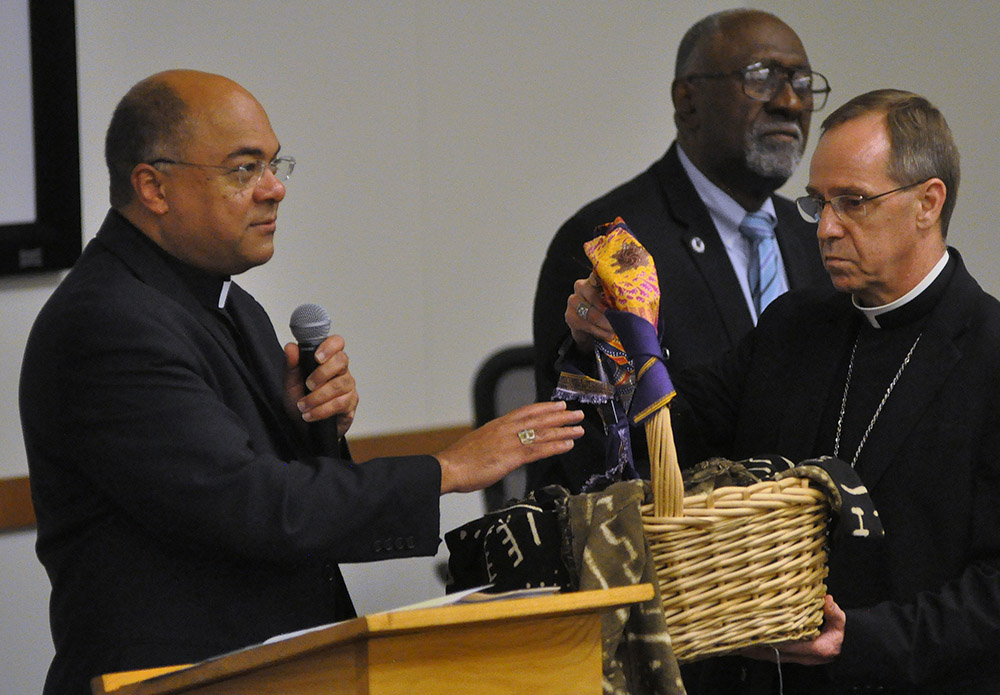 During a 2019 listening session on racism in Indianapolis, Bishop Shelton Fabre of Houma-Thibodaux, Louisiana, blesses a basket (held by Indianapolis Archbishop Charles Thompson) containing people's written accounts of experiences of racism. (CNS)