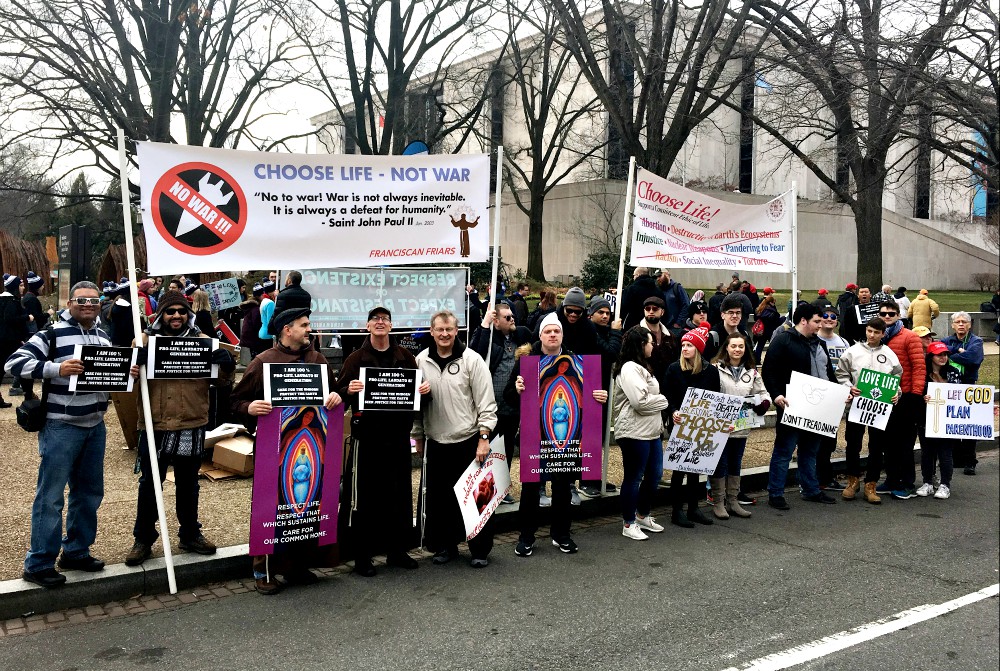 Franciscan friars and their supporters hold signs aloft outside of the security barrier where U.S. President Donald Trump spoke at the March for Life in Washington Jan. 24. (CNS/Courtesy of Lonnie Ellis)