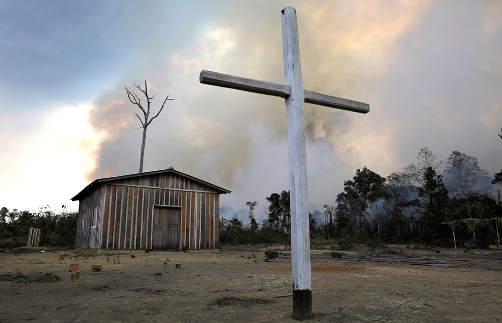 A wooden cross is seen in front of a Catholic church as a fire burns a tract of the Amazon jungle being cleared by loggers and farmers near Porto Velho, Brazil, Aug. 27, 2019. (CNS/Reuters/Ricardo Moraes)