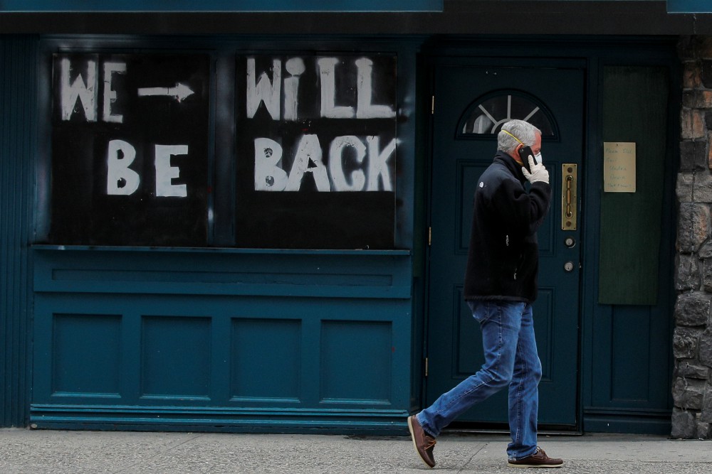 A man passes by a boarded-up restaurant in New York City April 29 with a sign suggesting it will reopen for business once it's safe in the coronavirus pandemic climate. (CNS/Reuters/Brendan McDermid)