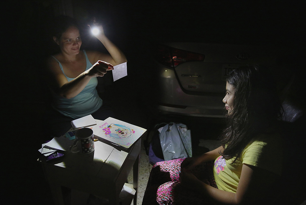 In this 2017 file photo, Margarita Rodriguez holds a flashlight as she quizzes her 11-year-old daughter Isel Martinez on homework outside their home in San Juan, Puerto Rico. (CNS/Bob Roller)
