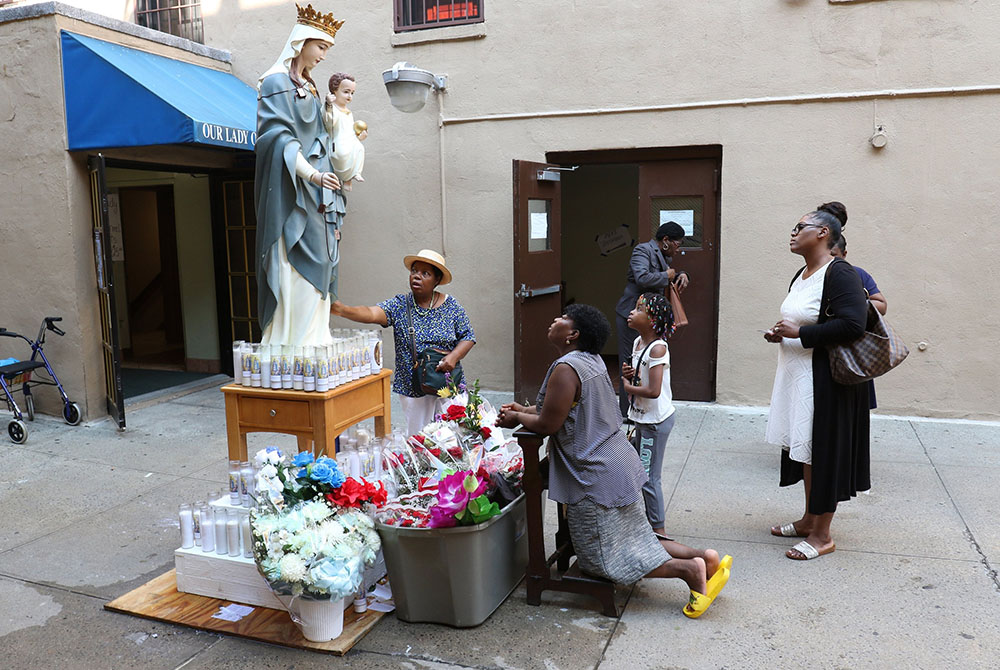People pray near a statue of Our Lady of Mount Carmel on her feast July 16, 2018, at the Pontifical Shrine of Our Lady of Mount Carmel in East Harlem, New York. Founded in 1884 to serve Italian immigrants, the parish now ministers to a congregation compri