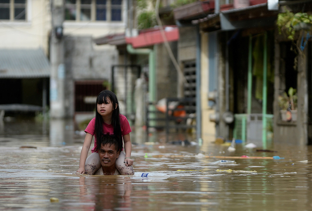 A man carries a child on his shoulders through a flooded street in Manila, Philippines, following Typhoon Vamco. (CNS/Reuters/Lisa Marie David)