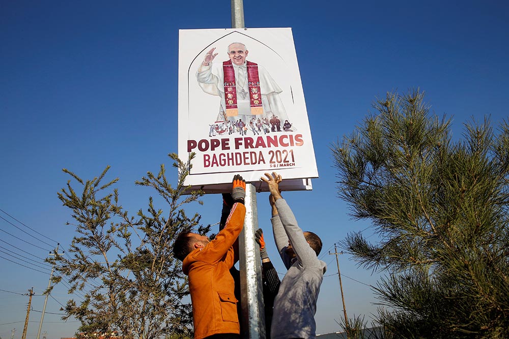 Volunteers secure a placard on a pole along a street in Qaraqosh, Iraq, Feb. 22. The placard shows the official logo, designed by Ragheed Nenwaya, for Pope Francis' planned March 7 visit to Qaraqosh, also known by its Aramaic name of Baghdeda.