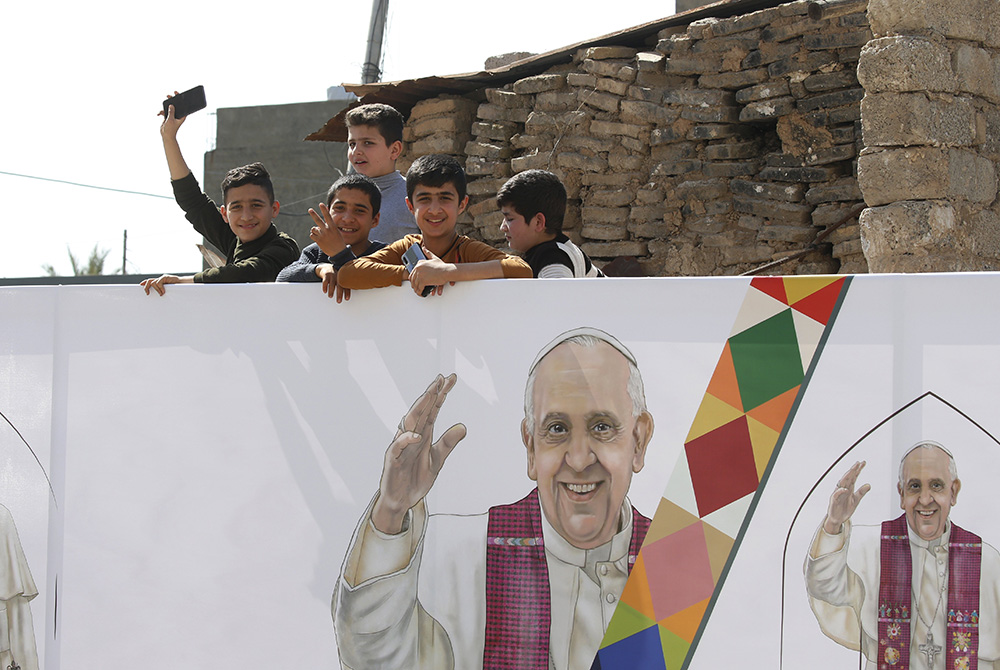 Children are seen near an image of Pope Francis during the pope's visit with the community at the Church of the Immaculate Conception March 7 in Qaraqosh, Iraq. (CNS/Paul Haring)