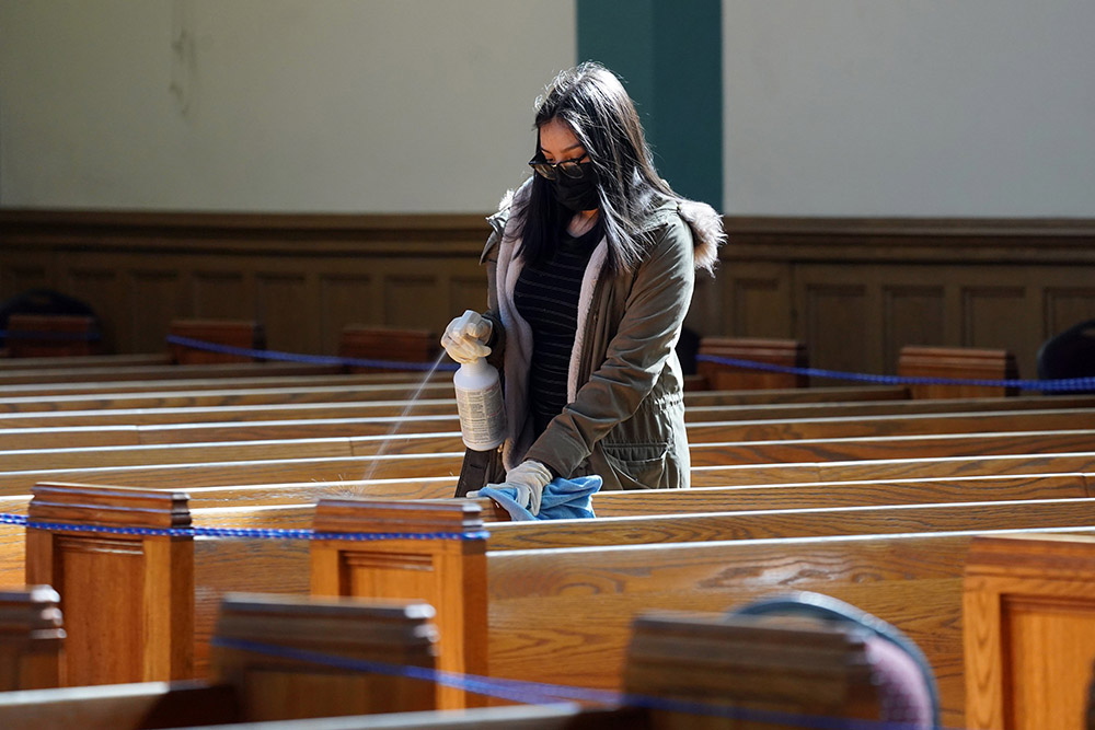 A young woman helps sanitize pews following a memorial Mass in English and Spanish on March 13 for parishioners who have died from COVID-19 at St. John-Visitation Church in the Bronx borough of New York. (CNS/Gregory A. Shemitz)