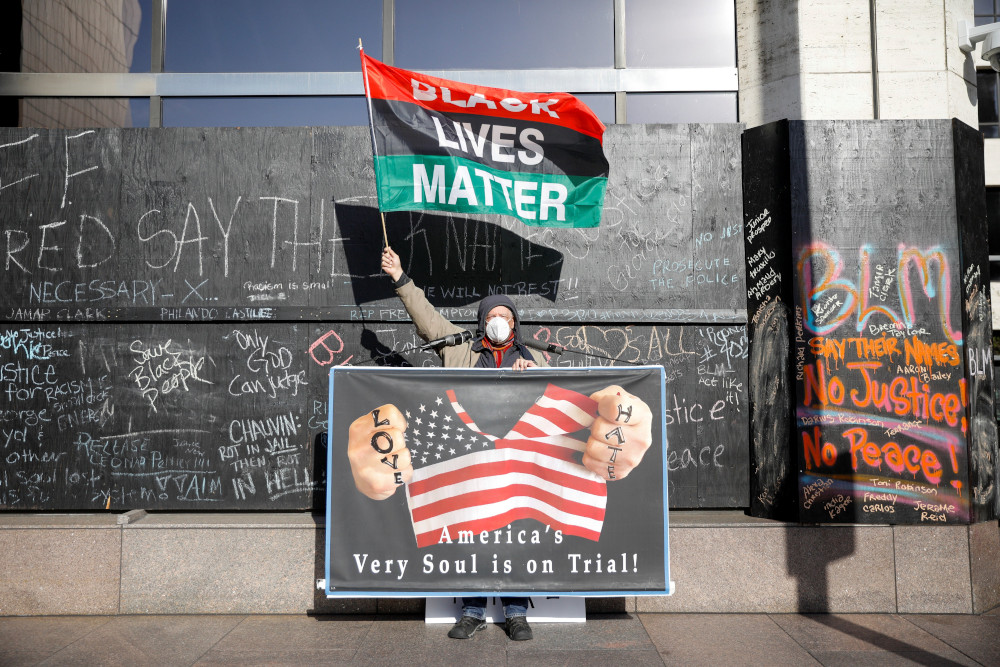 A demonstrator holds a "Black Lives Matter" flag and another sign outside the Hennepin County Government Center in Minneapolis April 6, 2021, the seventh day of the trial of former police officer Derek Chauvin. (CNS/Reuters/Nicholas Pfosi)