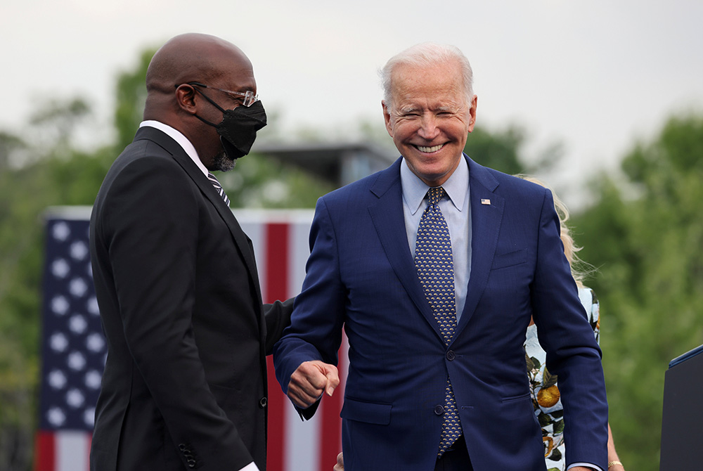 President Joe Biden smiles next to Sen. Raphael Warnock, D-Georgia, at the Infinite Energy Center April 29 in Duluth, Georgia, during the Democratic National Committee's "Back on Track" drive-in car rally to celebrate the president's 100th day in office. 