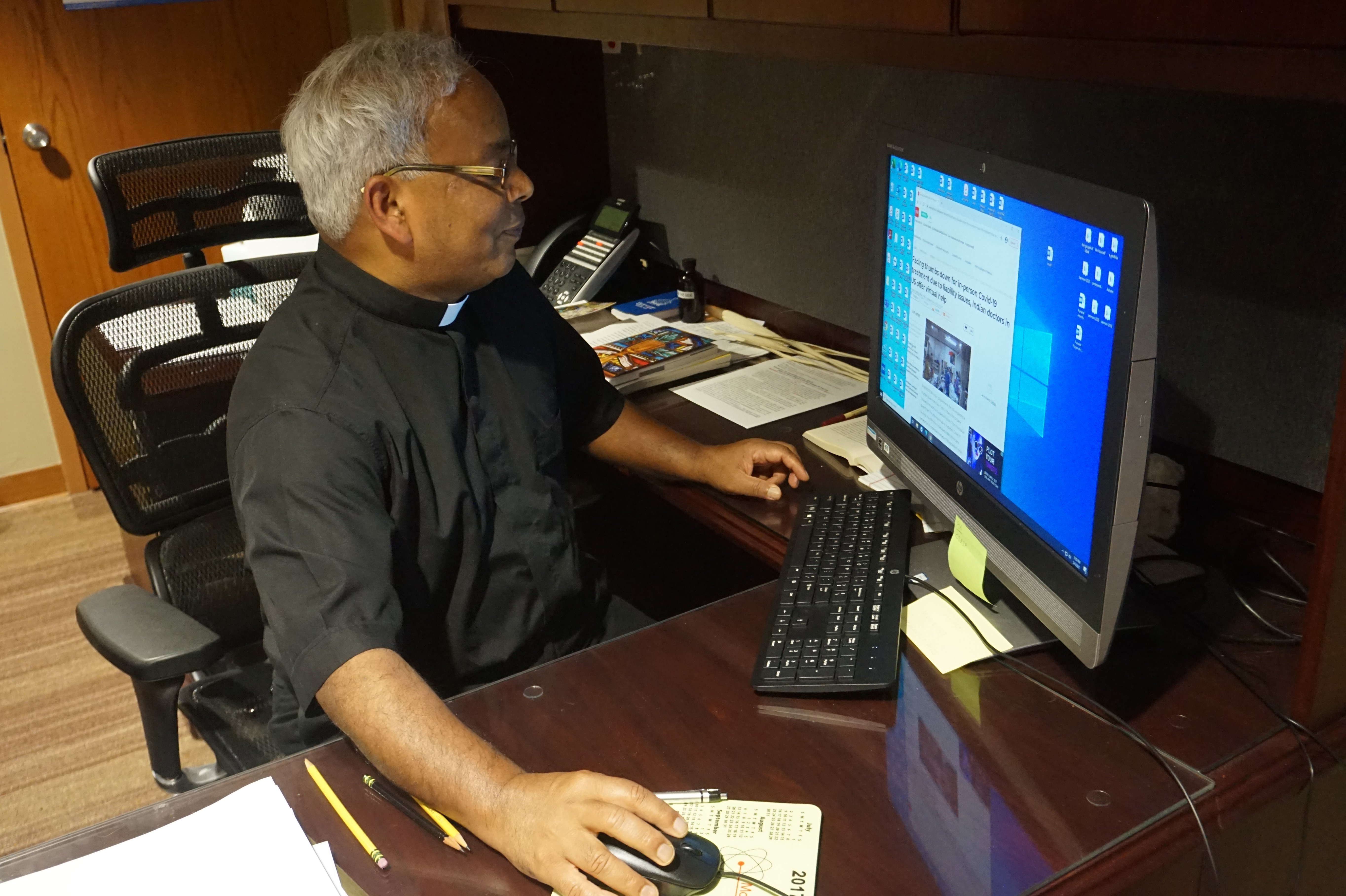 Father Aby Abraham, associate pastor at the Cathedral of St. Andrew in Little Rock, Ark., reads an India Times article about the ongoing COVID-19 crisis in India May 5, 2021. (CNS photo/Aprille Hanson Spivey, Arkansas Catholic)