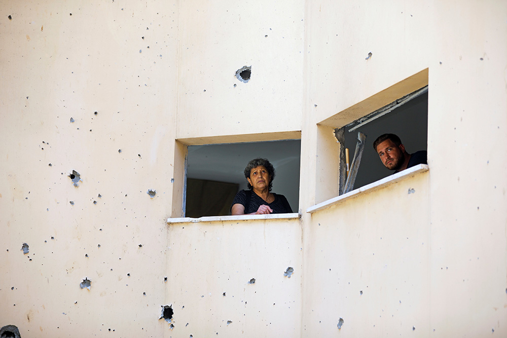 People look out May 20 in Petah Tikva, Israel, from a building damaged after a rocket fired from the Gaza Strip landed nearby. (CNS/Reuters/Nir Elias)