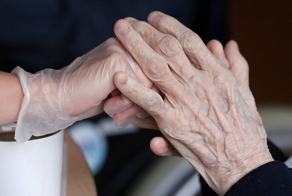 An employee holds the hand of a person at an elderly residence in Brussels April 14, 2020, during the COVID-19 pandemic. (CNS/Reuters/Yves Herman)