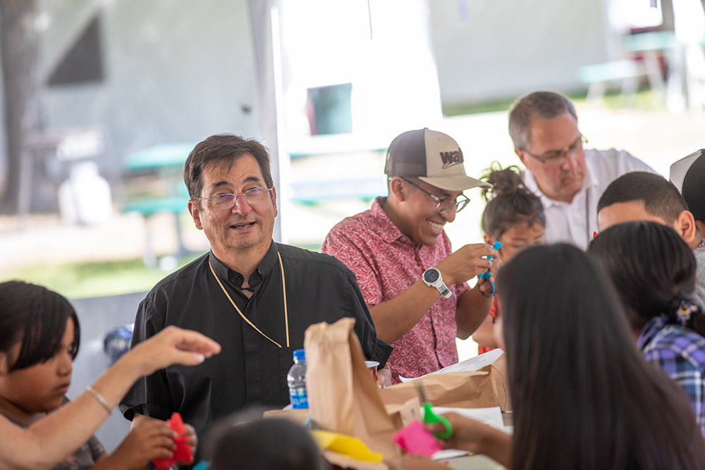 Bishop Joseph Tyson (left) of Yakima, Washington, leads migrant children in crafts July 29 as part of the Literacy Wagon program for migrant children whose parents are working in the fields. (Courtesy of Catholic Extension)