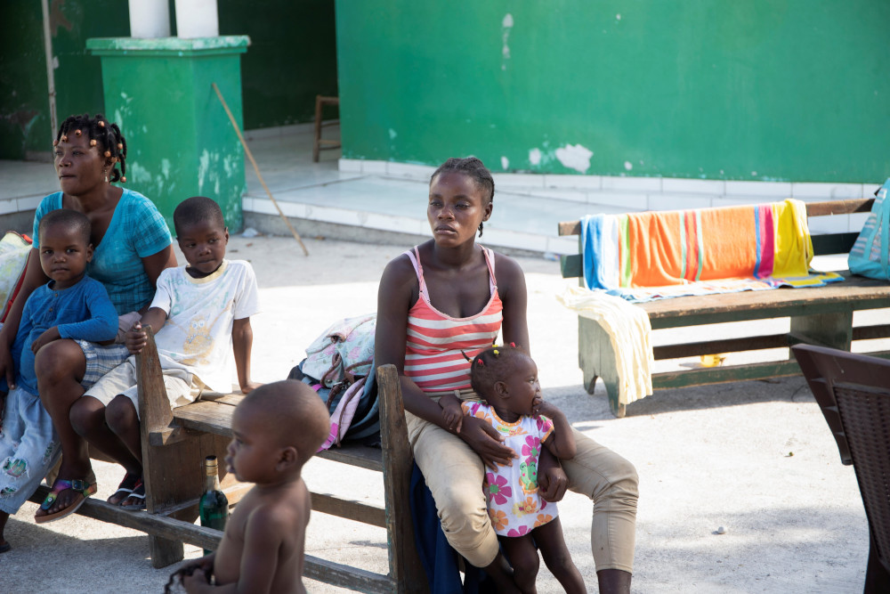 Women and children sit on a bench outside a building Aug. 15 in Les Cayes, Haiti, following a magnitude 7.2 earthquake the previous day. (CNS/Reuters/Estailove St-Val)