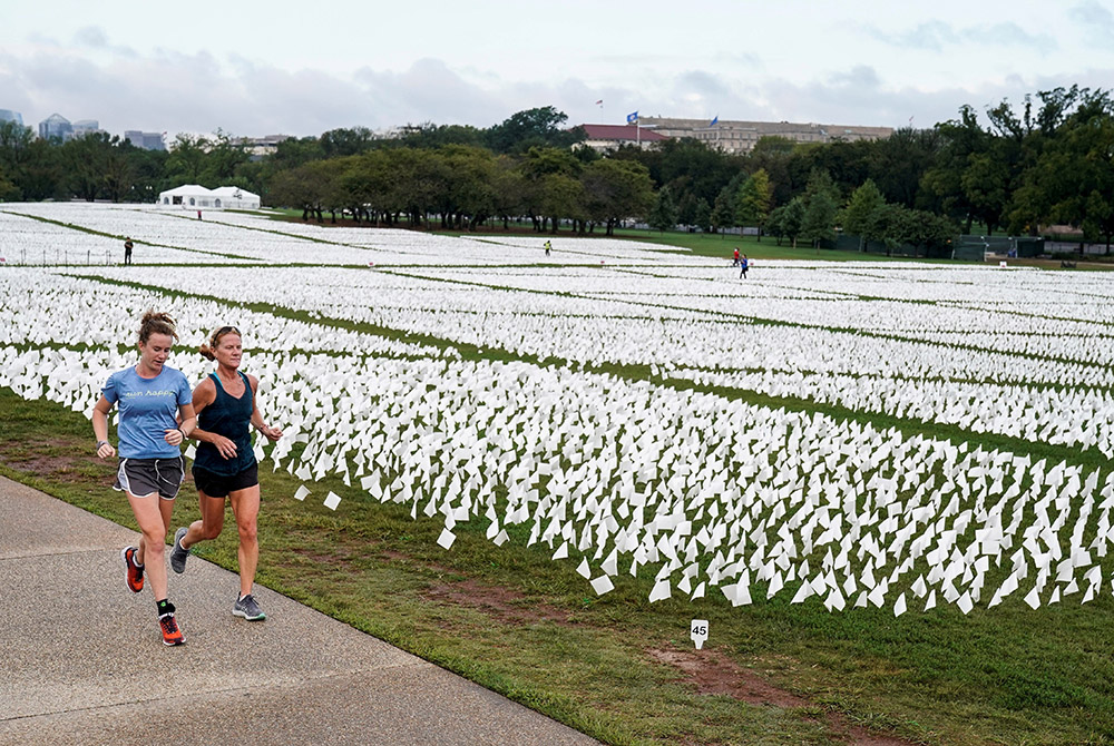 Women in Washington run past an exhibition of white flags at the National Mall Sept. 17, that represent Americans who have died of the coronavirus disease. (CNS/Reuters/Joshua Roberts)