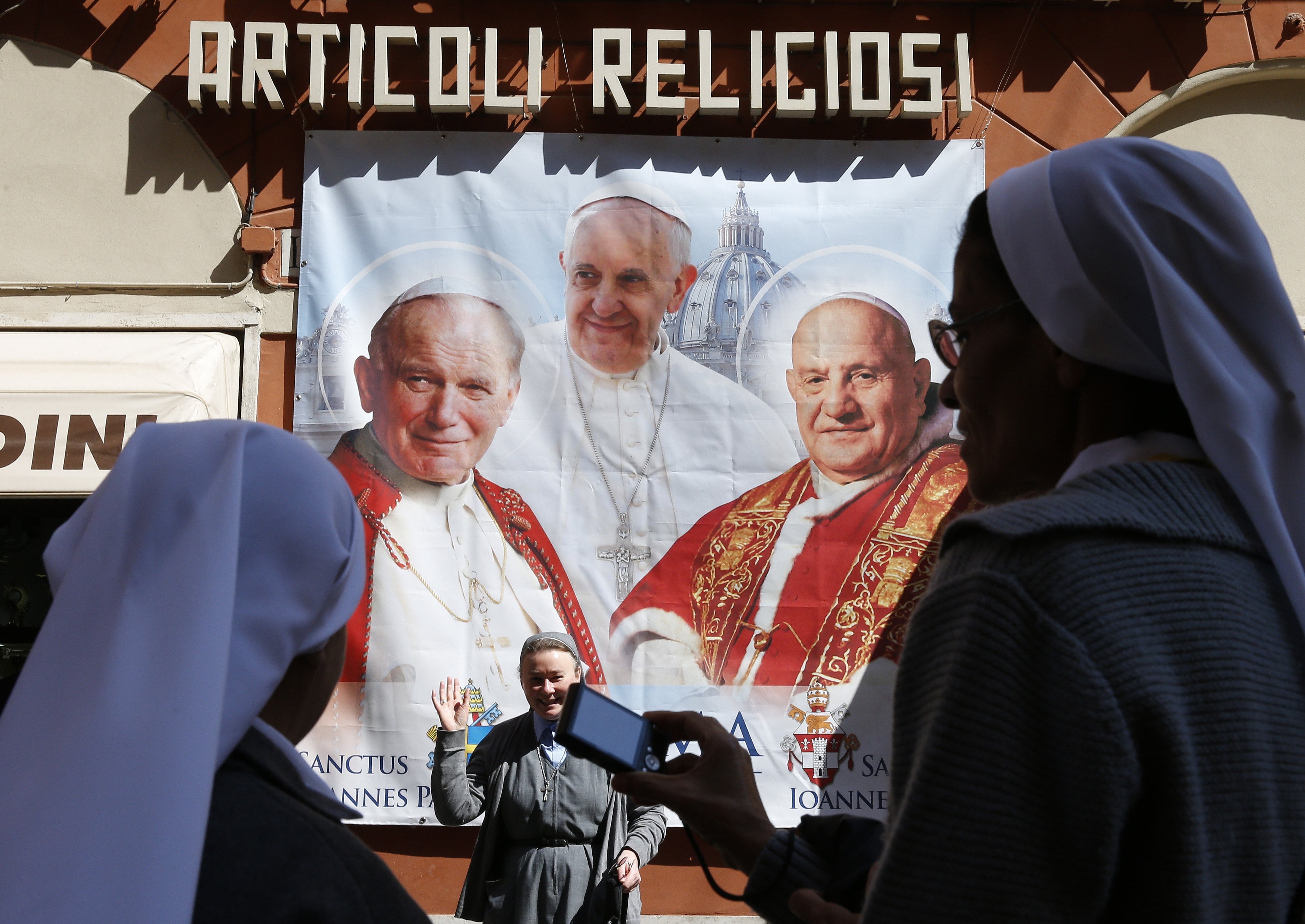 Nuns from Brazil take photos in front of a large banner of Pope Francis, then-Blesseds John XXIII and John Paul II in Rome in this April 25, 2014, file photo. With the news that Pope John Paul I will be beatified, some have begun to wonder if being pope i