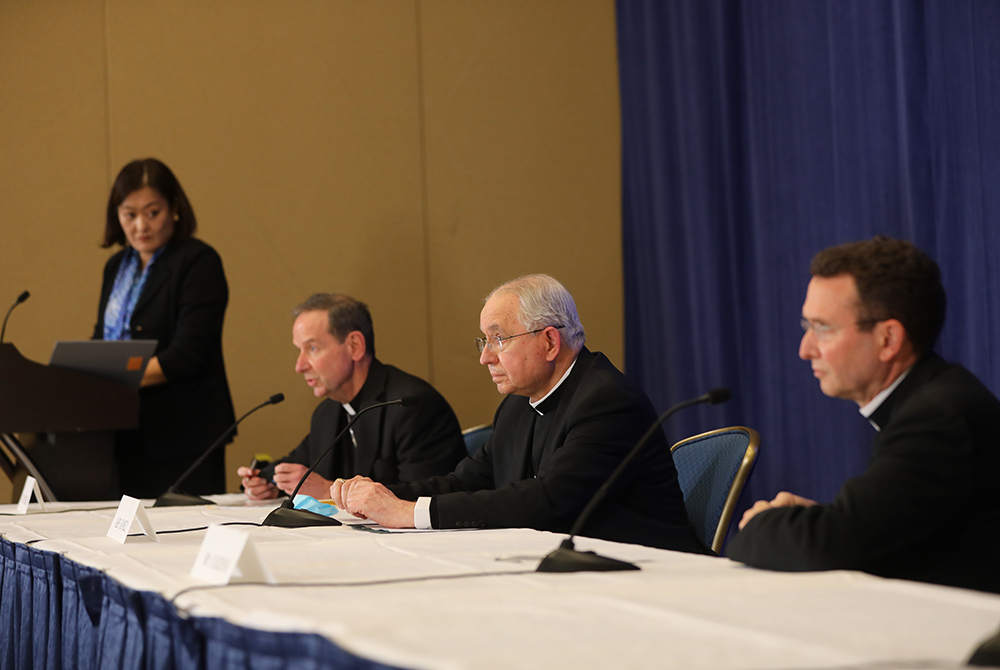 Bishop Michael Burbidge, Archbishop José Gomez , president of the U.S. bishops' conference, and Auxiliary Bishop Andrew Cozzens attend a Nov. 16 news conference during the bishops' fall assembly in Baltimore. At the podium is Chieko Noguchi. (CNS)