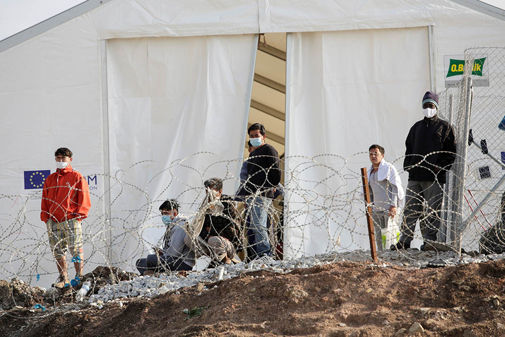 Refugees and migrants stand next to a tent in the Mavrovouni camp on the island of Lesbos, Greece, March 29. (CNS/Reuters/Elias Marcou)