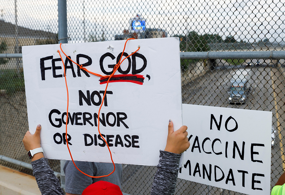 People raise signs against a chain-link fence to show drivers on Ohio state Route 8 during an Aug. 16 protest against the COVID-19 vaccine mandates at Summa Health Hospital in Akron, Ohio. (CNS/Reuters/Stephen Zenner)
