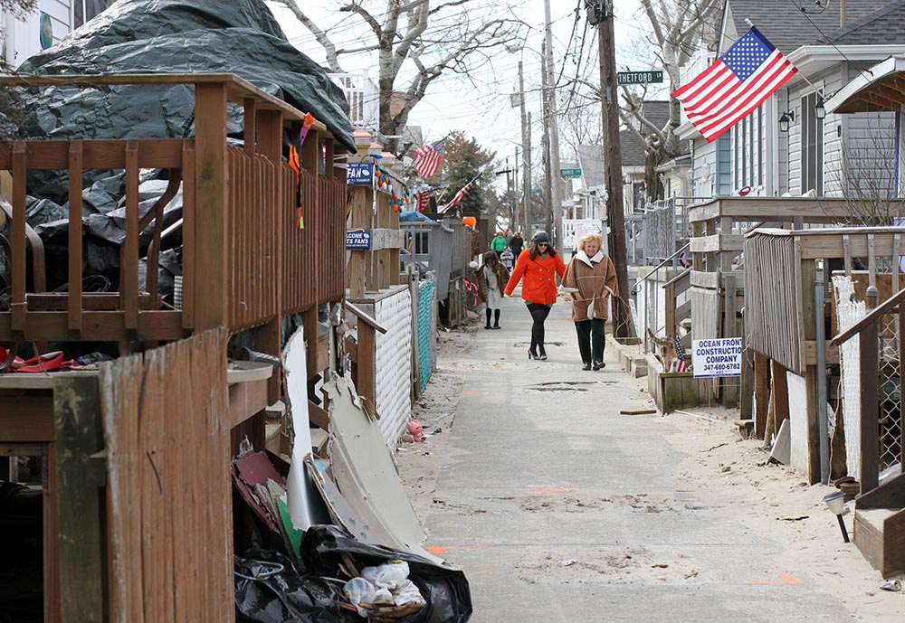 People walk along a sidewalk between damaged homes in the Breezy Point section of the New York borough of Queens March 17, 2013. Breezy Point was devastated by fire and flooding when Hurricane Sandy swept through the region in October 2012. (CNS/Gregory A. Shemitz)