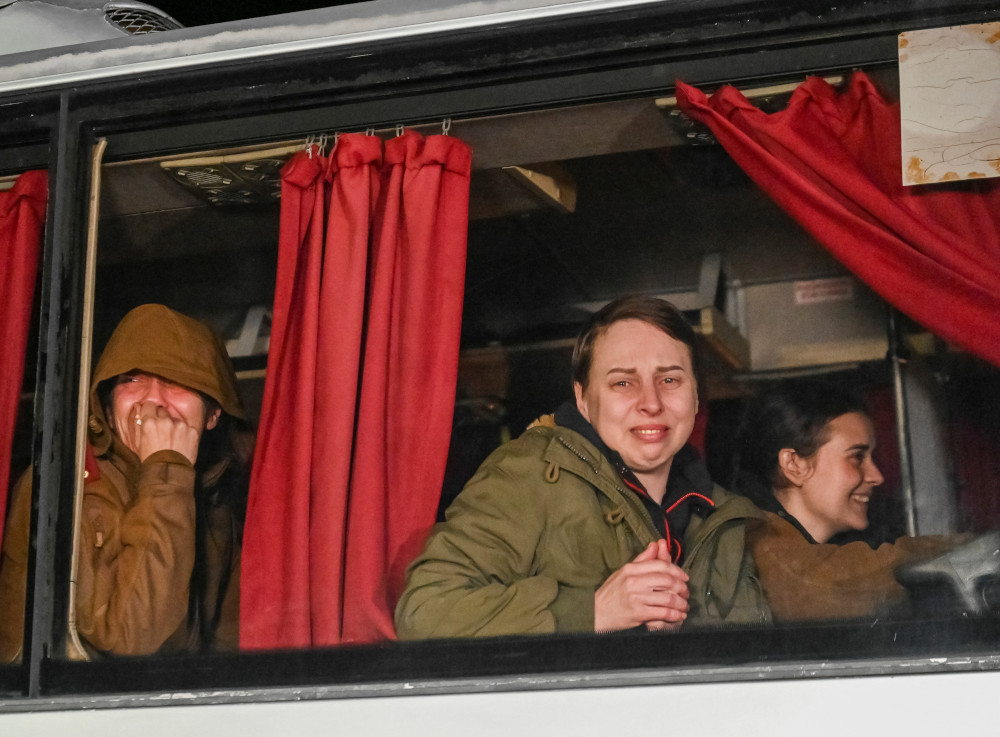 Ukrainian women wearing green coats stare emotionally out of windows on a bus or train