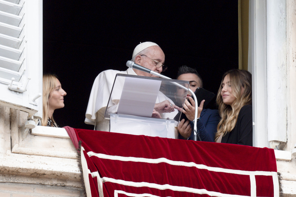 Young people from Portugal join Pope Francis in the window of his studio overlooking St. Peter's Square Oct. 23, 2022, as they help him use a tablet to be the first to register to attend World Youth Day 2023 in Lisbon.