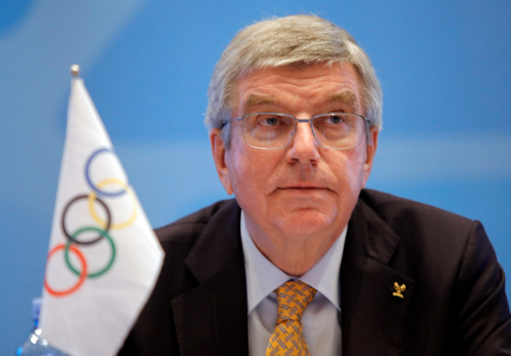 Thomas Bach sits behind a small flag with the Olympic rings